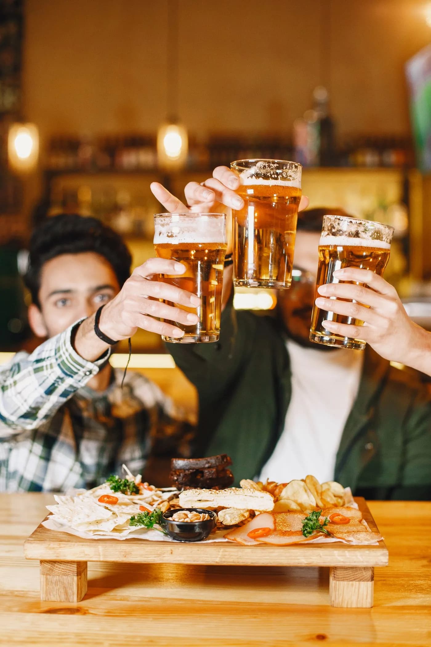 Symbolfoto: Freunde stoßen mit Biergläsern an einem gedeckten Tisch an